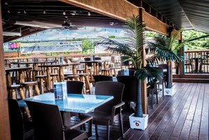 An outdoor restaurant with wooden tables and chairs, a covered seating area, and potted plants.