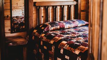 A wooden cabin room with a bed, a chair, and a mirror on the wall.