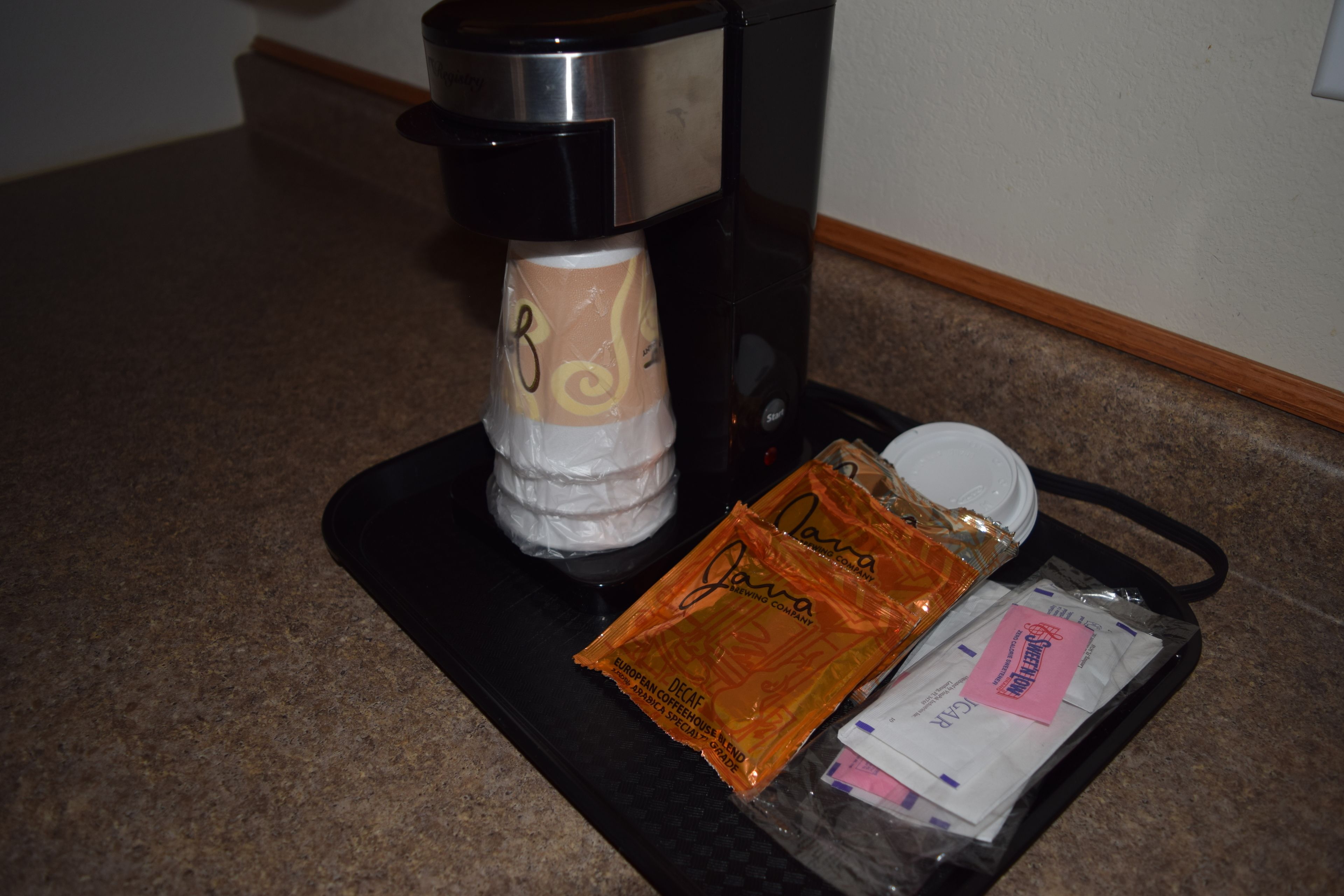 Uma cafeteira, uma cápsula de café e uma chávena descartável numa bancada.