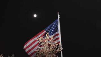 Una bandera estadounidense en un asta con un cielo nocturno y una luna visible.