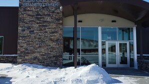 The exterior of the Killdeer Aquatics & Wellness Center with a stone facade and a glass entrance. - Mountain View Hotel (Killdeer)