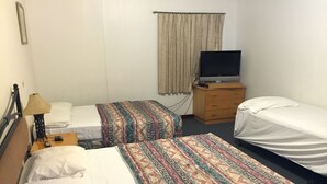 Ett hotellrum med två separata sängar, en tv på en byrå i trä, en lampa och en gardin.