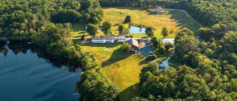 A large estate with a main house, guest house, and swimming pool surrounded by lush greenery and a lake.