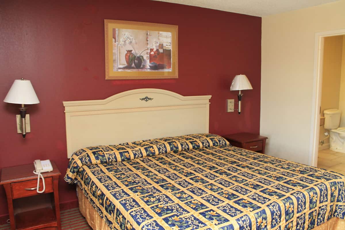 Quarto de hotel com uma cama grande, duas luminárias de cabeceira, um telefone num criado-mudo e um quadro na parede.