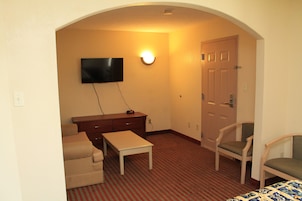 Habitación de hotel con televisor de pantalla plana montado en la pared, un escritorio de madera, una silla, un sofá y una puerta.