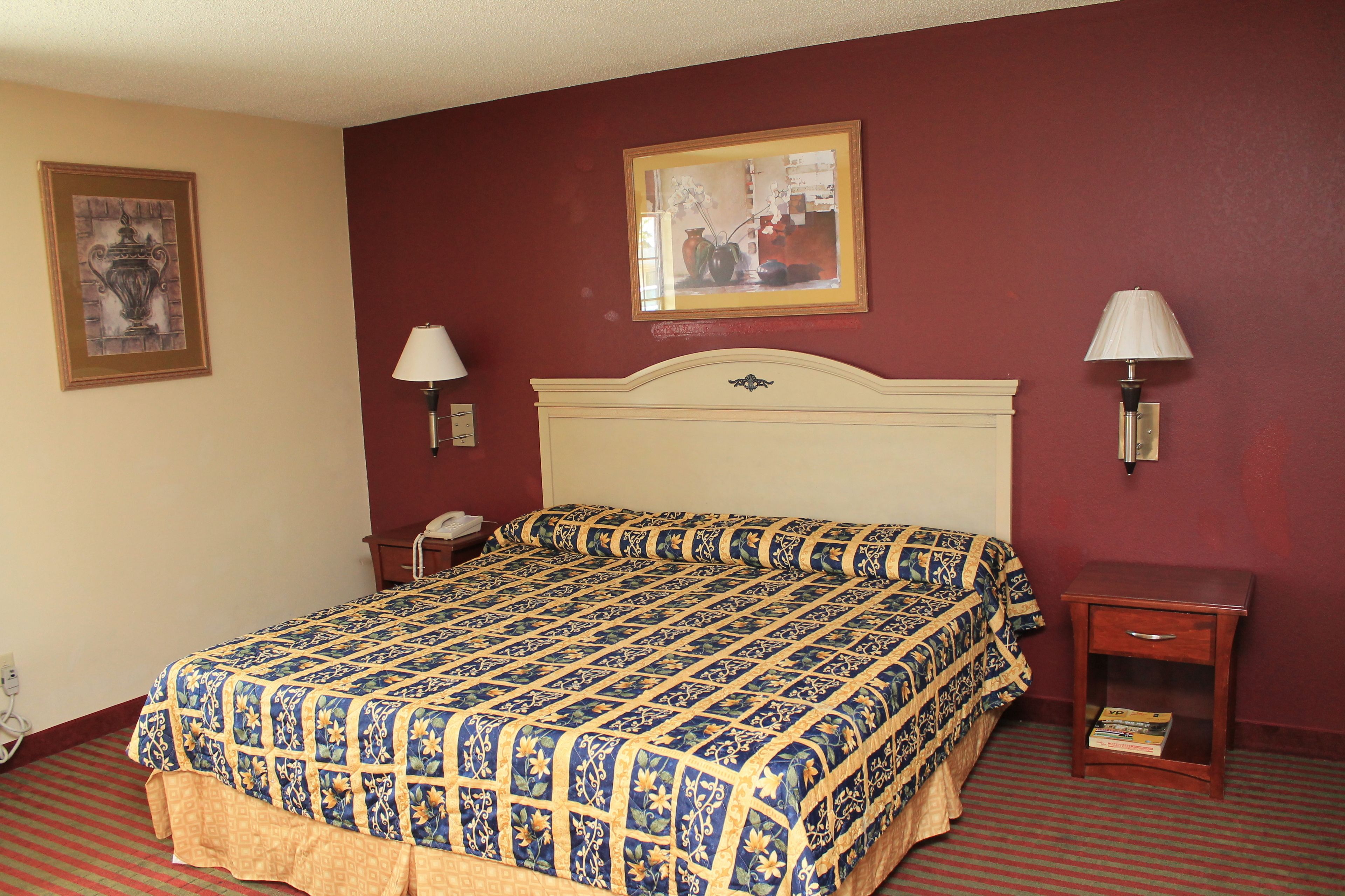 A hotel room with a large bed, two bedside tables, a nightstand, a framed picture on the wall, and a lamp on each bedside table.