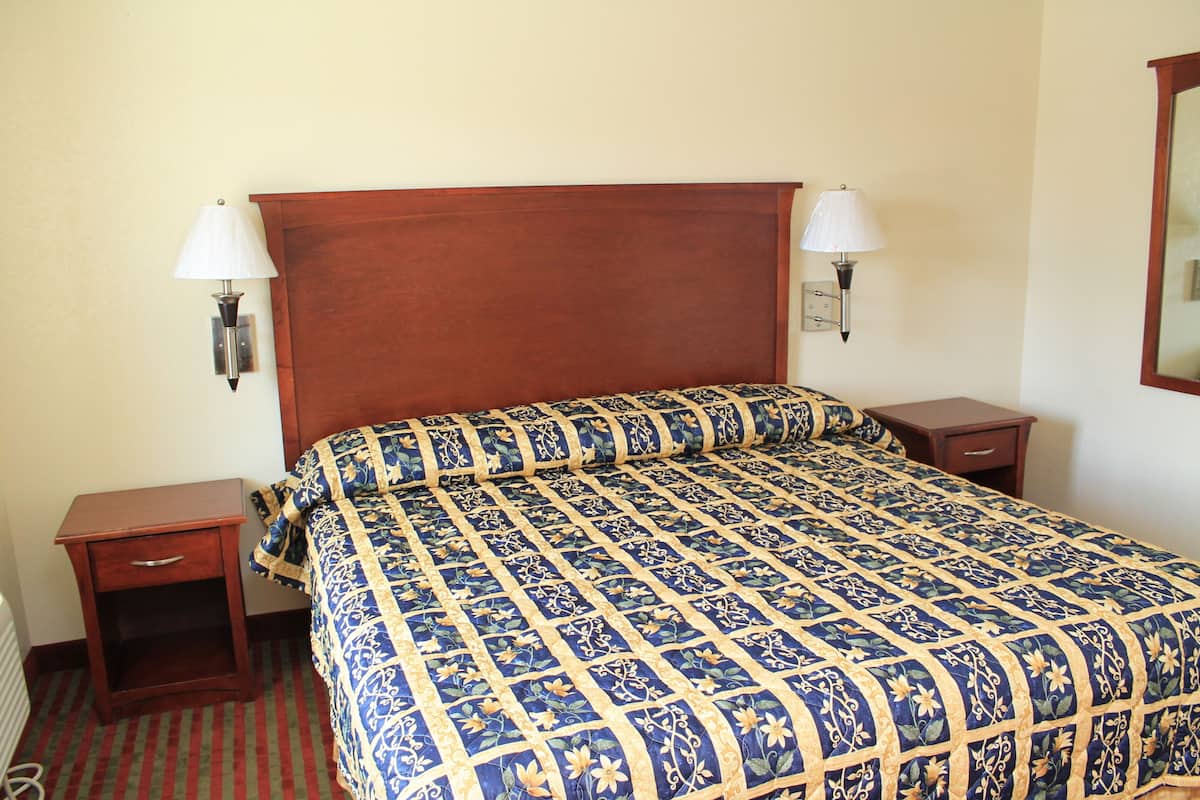 Quarto de hotel com uma cama grande, duas mesas de cabeceira e duas luminárias fixadas na parede.