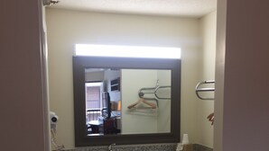 A bathroom with a granite countertop, a sink, a mirror, and a towel rack. - Travel Inn (Lugoff)