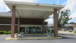 A hotel entrance with a covered walkway, brick pillars, and potted plants. - Travel Inn (Lugoff)