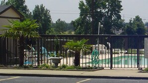 A fenced outdoor area with a pool, a building, and some greenery. - Travel Inn (Lugoff)