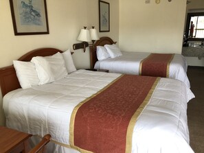 A hotel room with two beds, a wooden headboard, a nightstand, a lamp, and a framed picture on the wall.