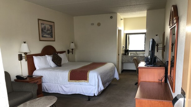 A hotel room with a bed, bedside tables, a desk, a chair, a television, and a bathroom visible through an open door. - Travel Inn (Lugoff)