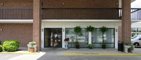 Un edificio de dos pisos con fachada de ladrillo, entrada porticada y plantas en macetas.
