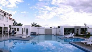 Un hotel moderno con piscina, sillones de descanso y cielo despejado.