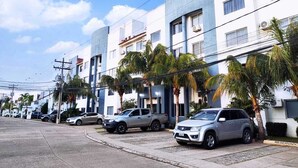 Una calle residencial con edificios modernos, coches estacionados y palmeras.