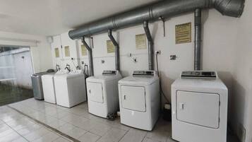 Une buanderie équipée de quatre machines à laver et dotée d’une grande conduite de ventilation située au-dessus.