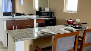 Una cocina con encimeras de granito, sillas de madera, microondas y ventana.