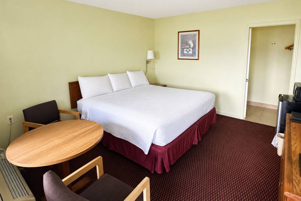 A hotel room with a bed, a desk, a chair, a lamp, and a picture on the wall.