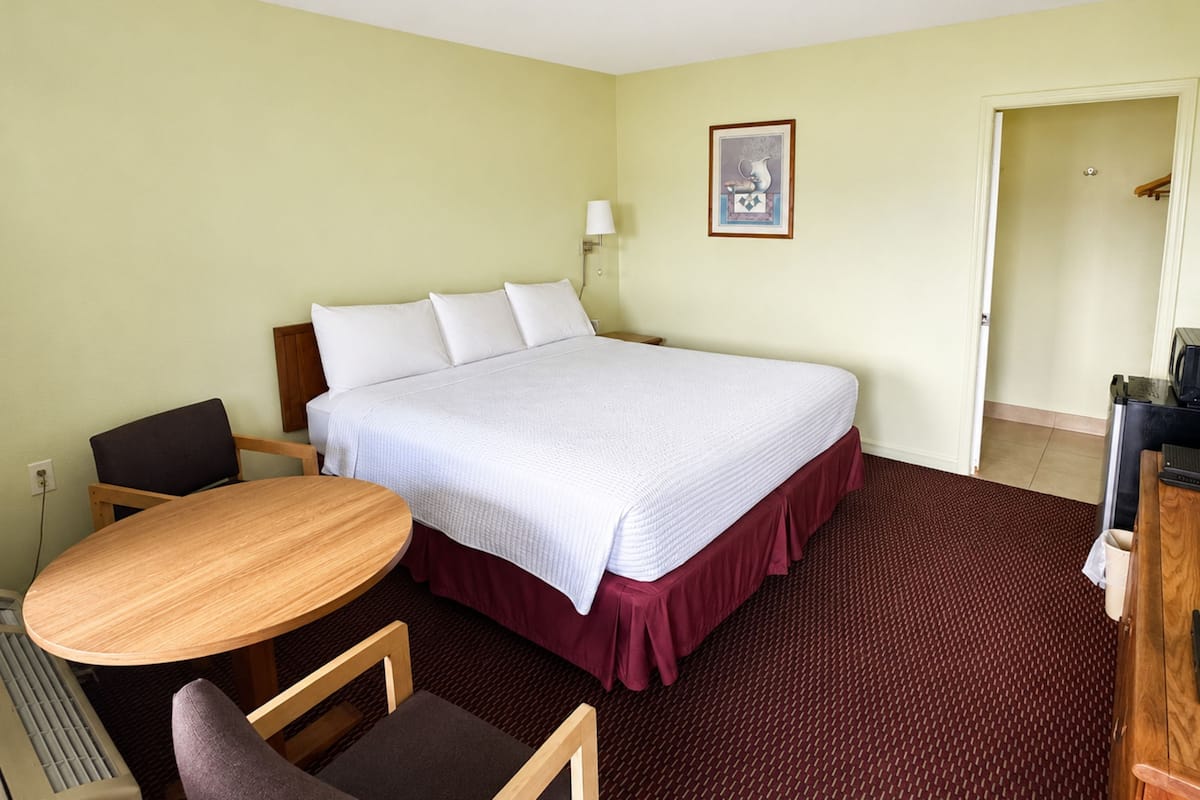 Ein Hotelzimmer mit Bett, Schreibtisch, Sessel, Lampe und einem Bild an der Wand.
