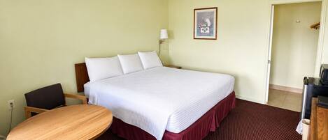 Habitación de hotel con cama, escritorio, silla, lámpara y un cuadro en la pared.