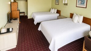 A hotel room with two beds, a desk, a chair, a lamp, and a small table.