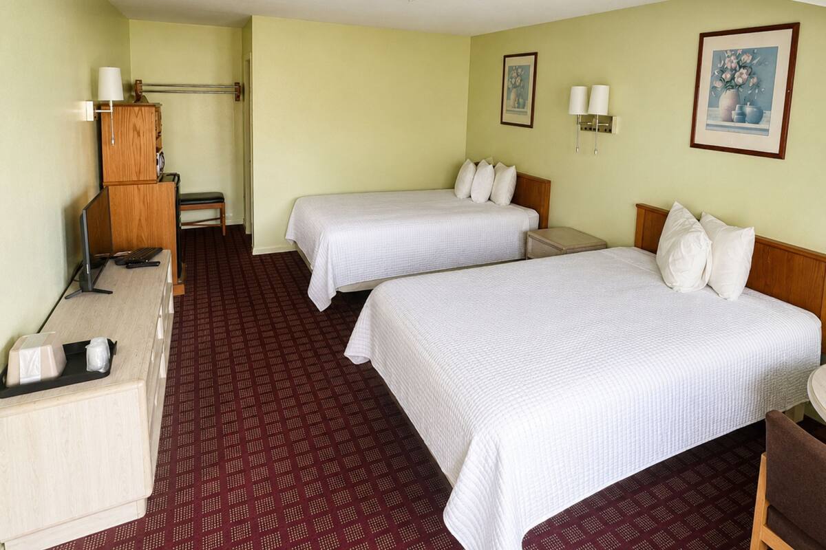 A hotel room with two beds, a desk, a chair, a lamp, and a small table.