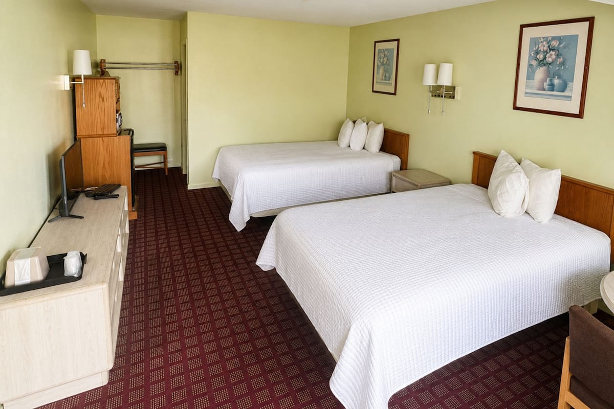 Ein Hotelzimmer mit zwei Betten, einem Schreibtisch, einem Stuhl, einer Lampe und einem kleinen Tisch.