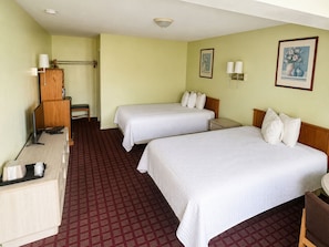 Ein Hotelzimmer mit zwei Betten, einem Schreibtisch, einem Stuhl, einer Lampe und einem kleinen Tisch.