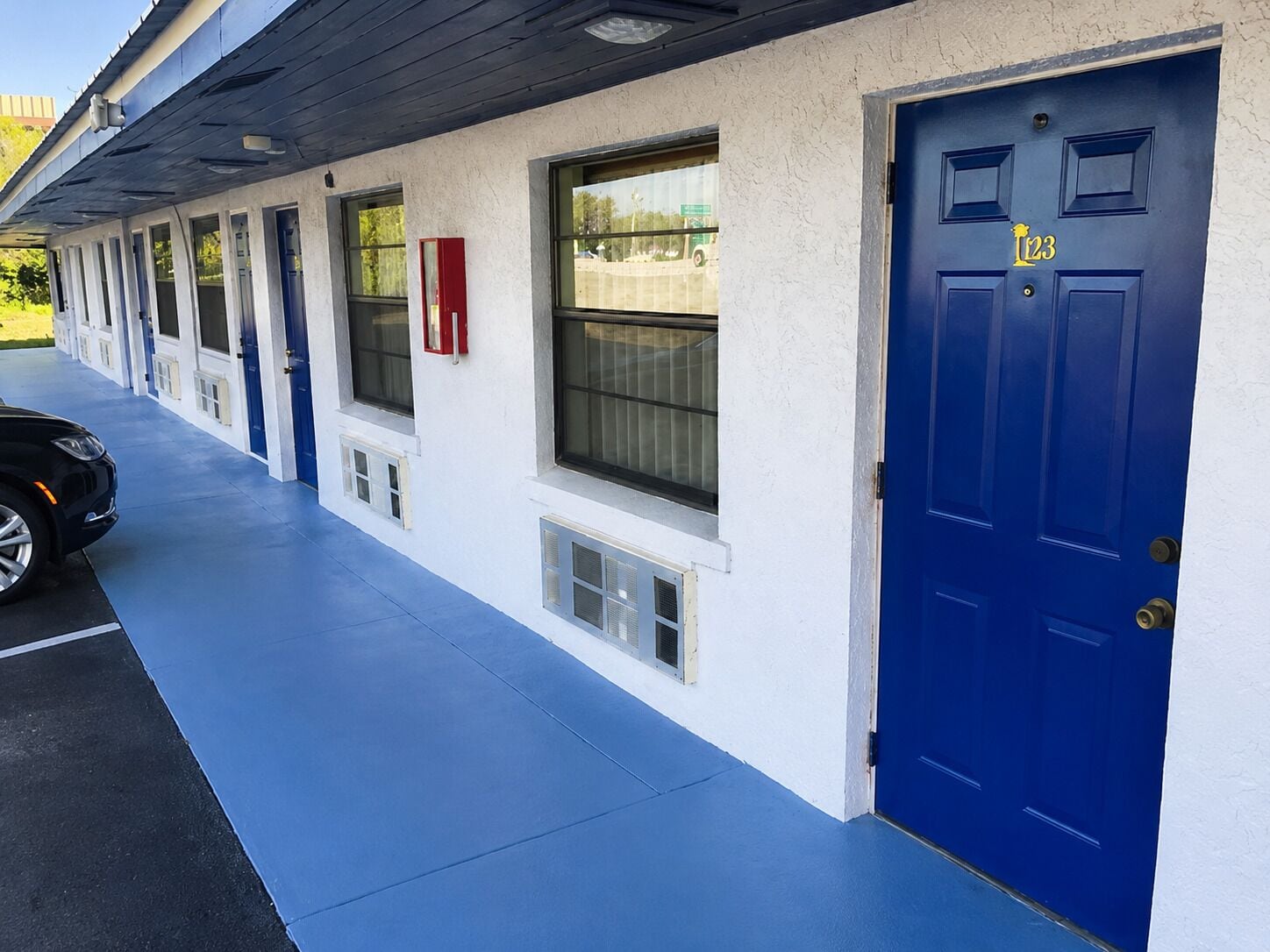 A building with a row of rooms, a blue door, and a car parked in front.