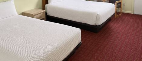 A hotel room with two beds, a desk, a chair, a lamp, and a window with curtains.