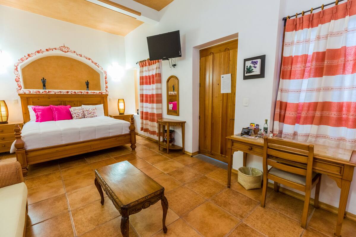 A bedroom with a wooden bed, a desk, a chair, a television, and a wooden door.