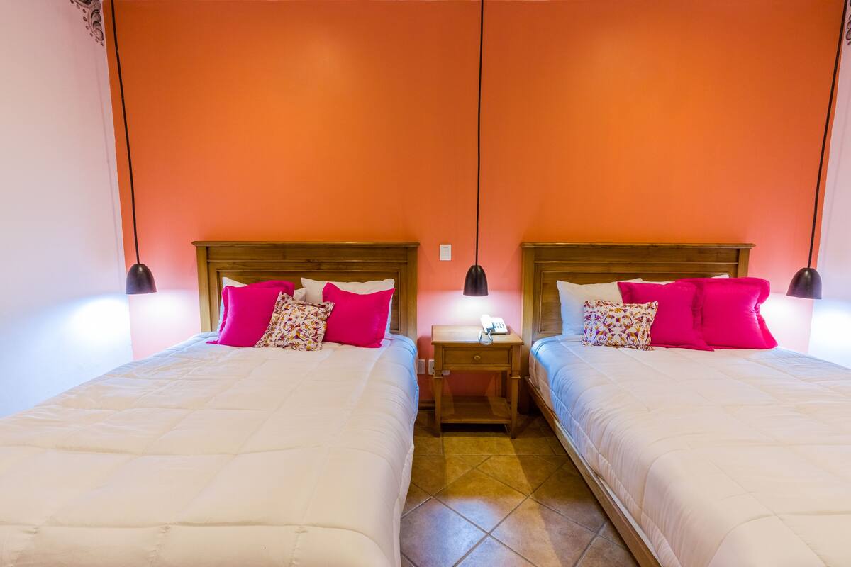 A double room with two beds, each with a wooden headboard, a nightstand with a lamp, and a telephone.