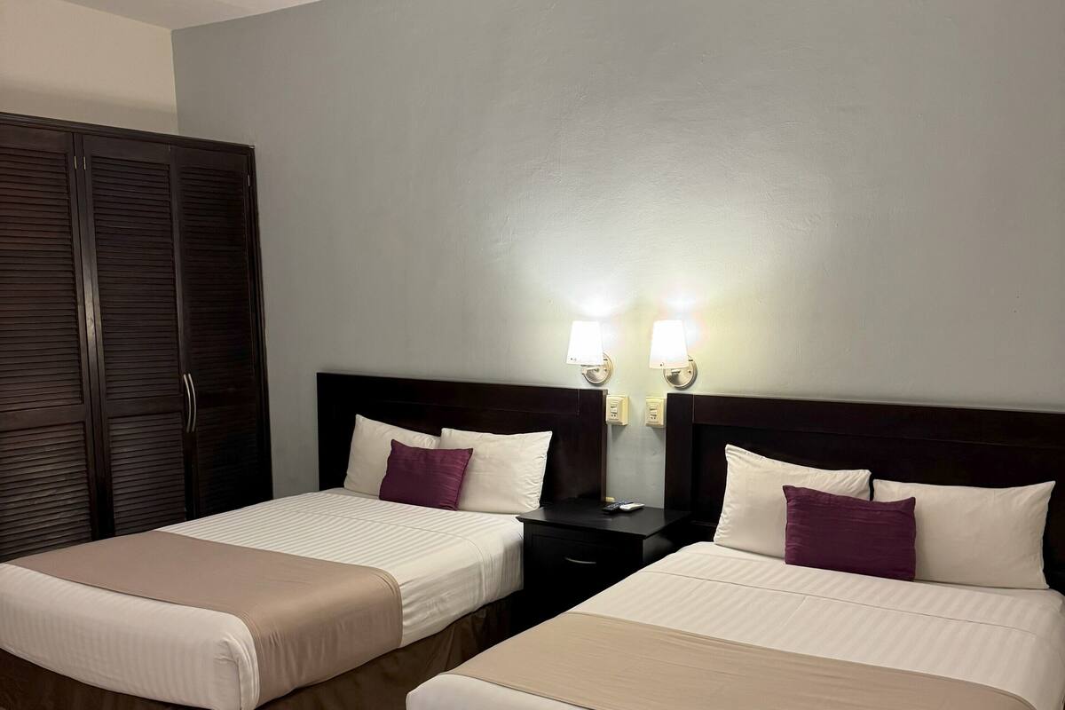 A hotel room with two beds, a wardrobe, and bedside lamps.