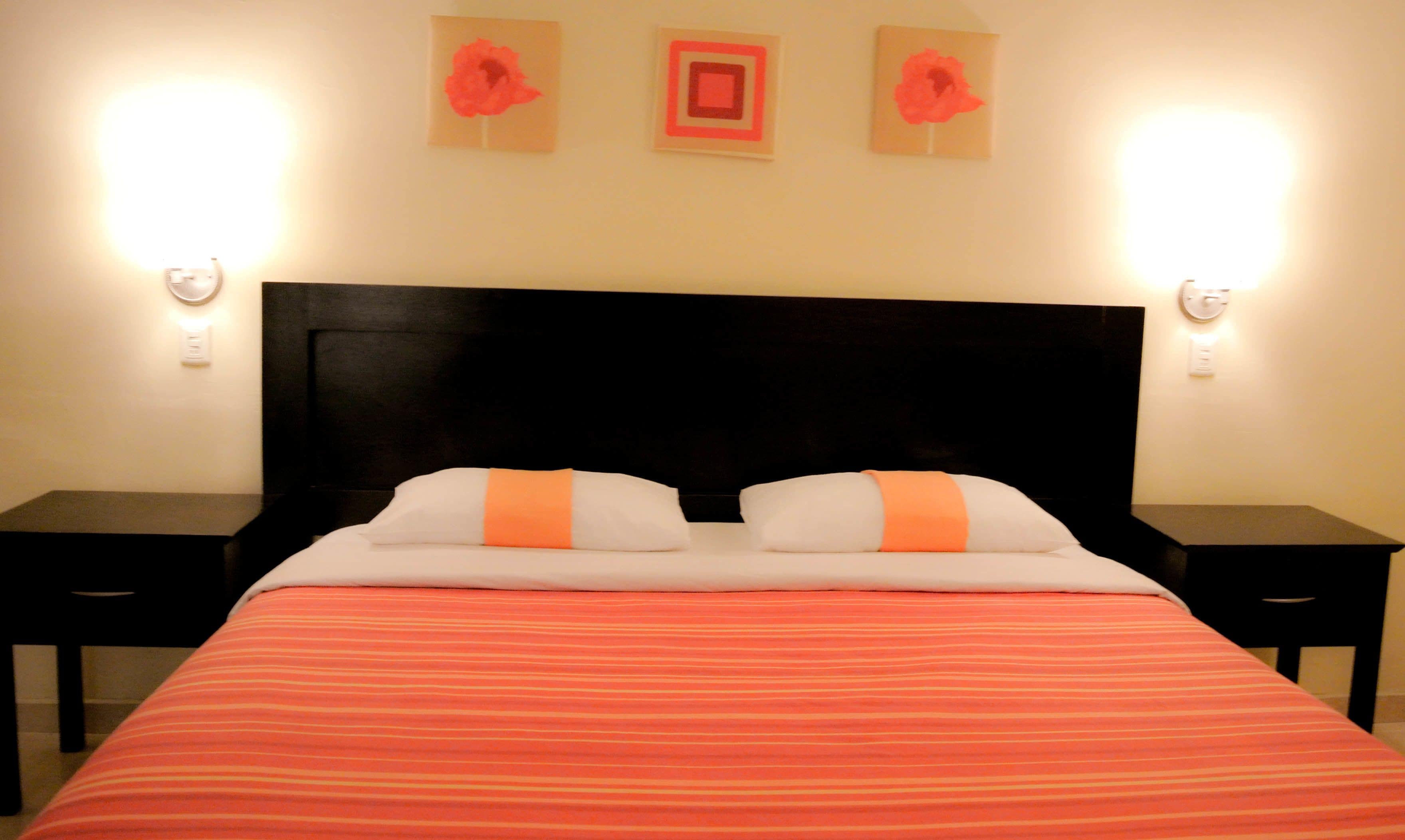 A bed with a striped red and white bedspread, two white pillows with orange accents, and a dark headboard. There are two bedside tables on either side of the bed.