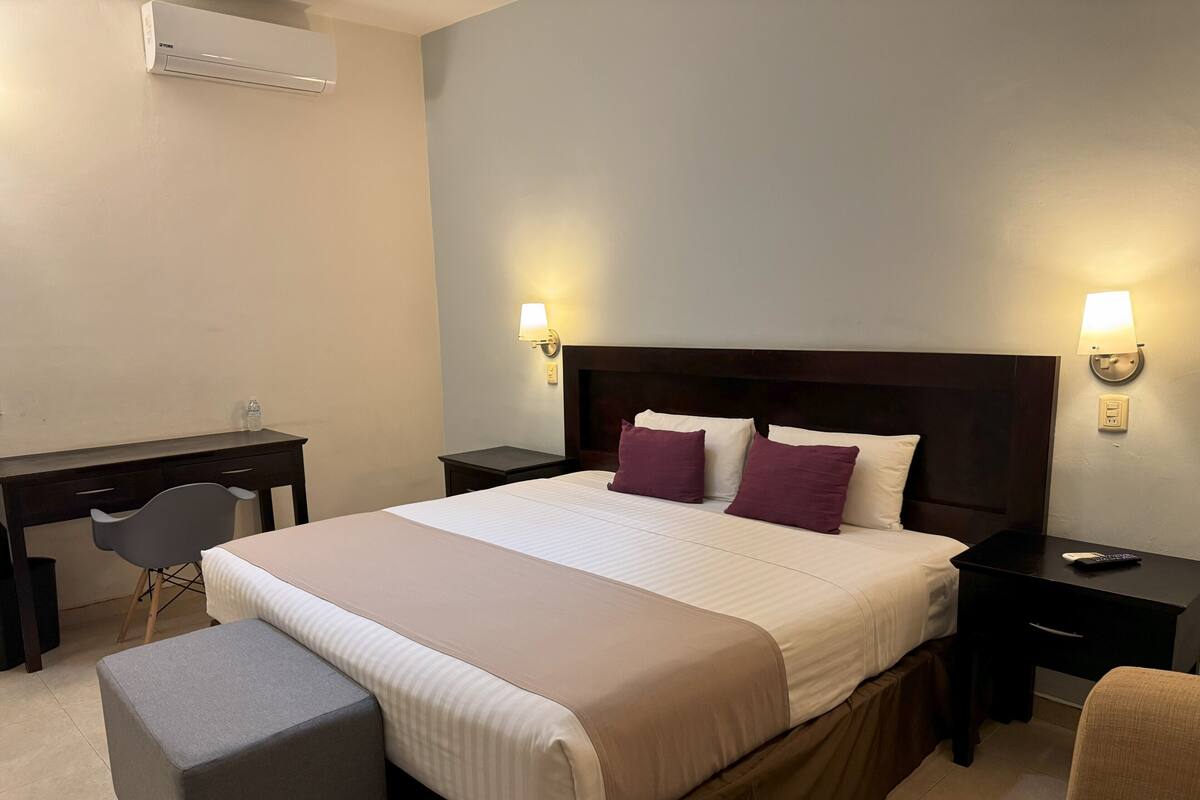 A hotel room with a large bed, a desk, a chair, and a small ottoman.