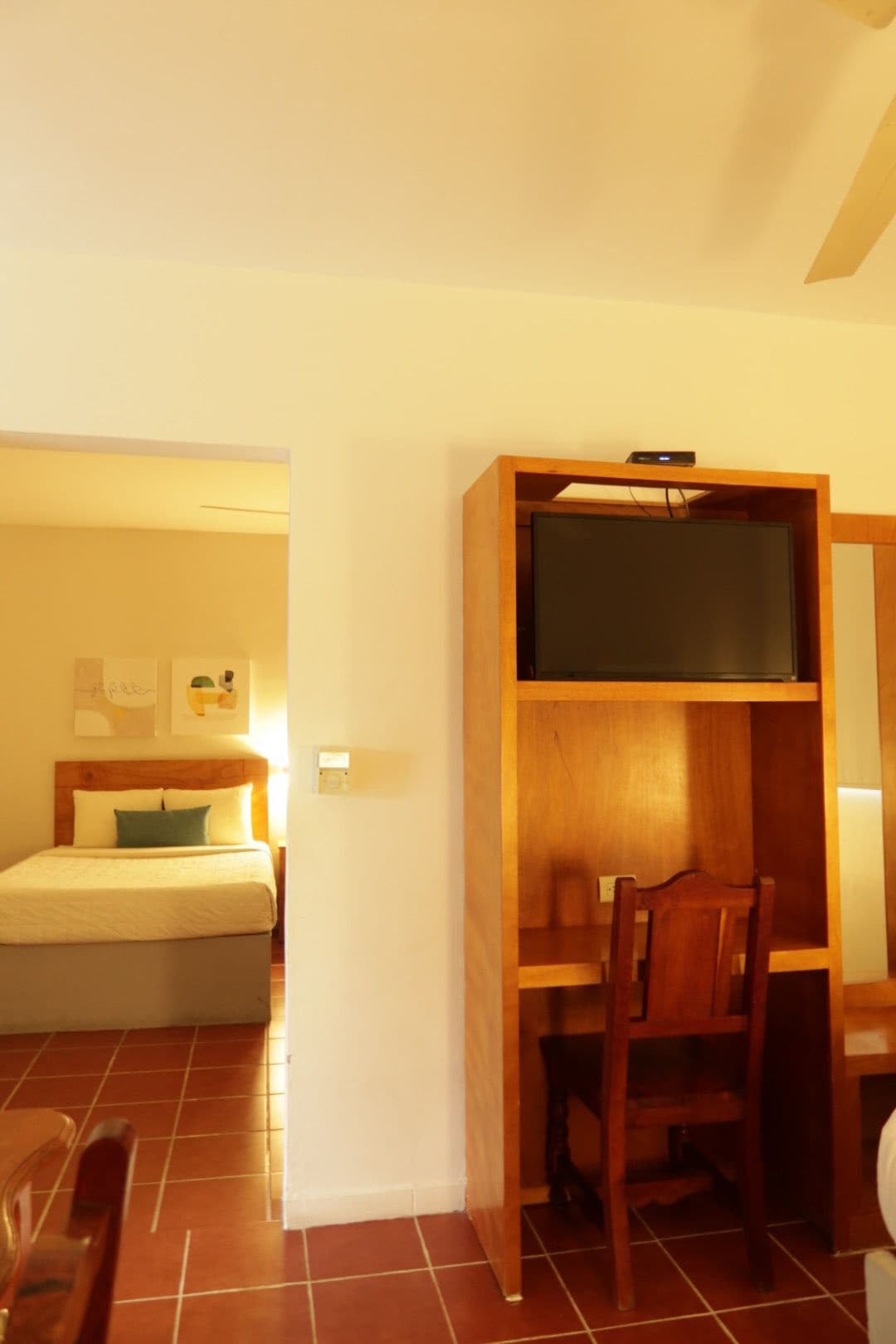 Un dormitorio con cama, un escritorio de madera y televisor sobre un mueble.