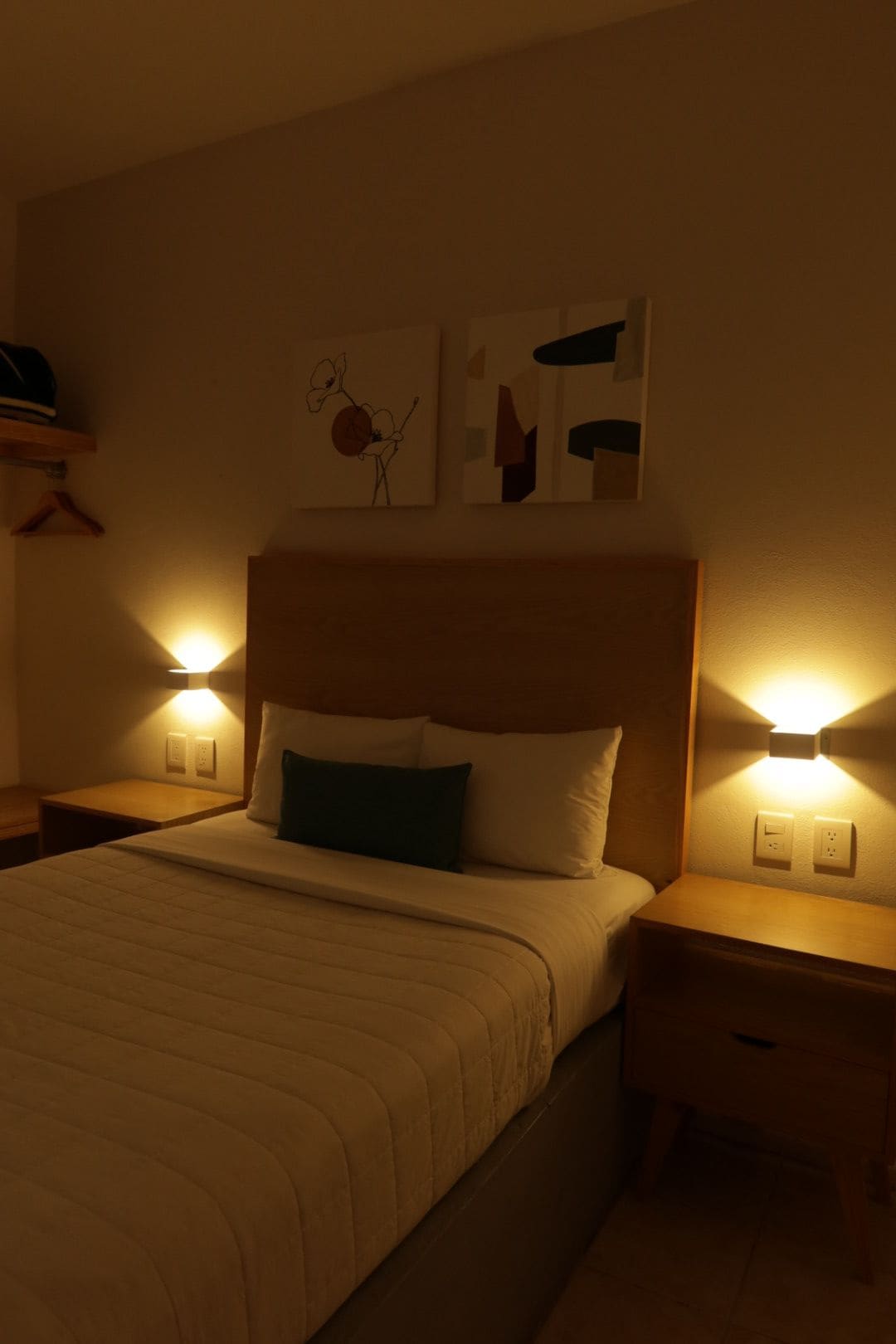 A hotel room with a bed, two bedside tables, and wall-mounted light fixtures.