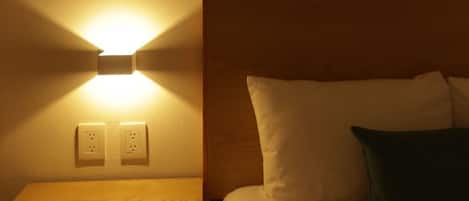 A hotel room with a bed, a bedside table, a wall-mounted light, and a painting.