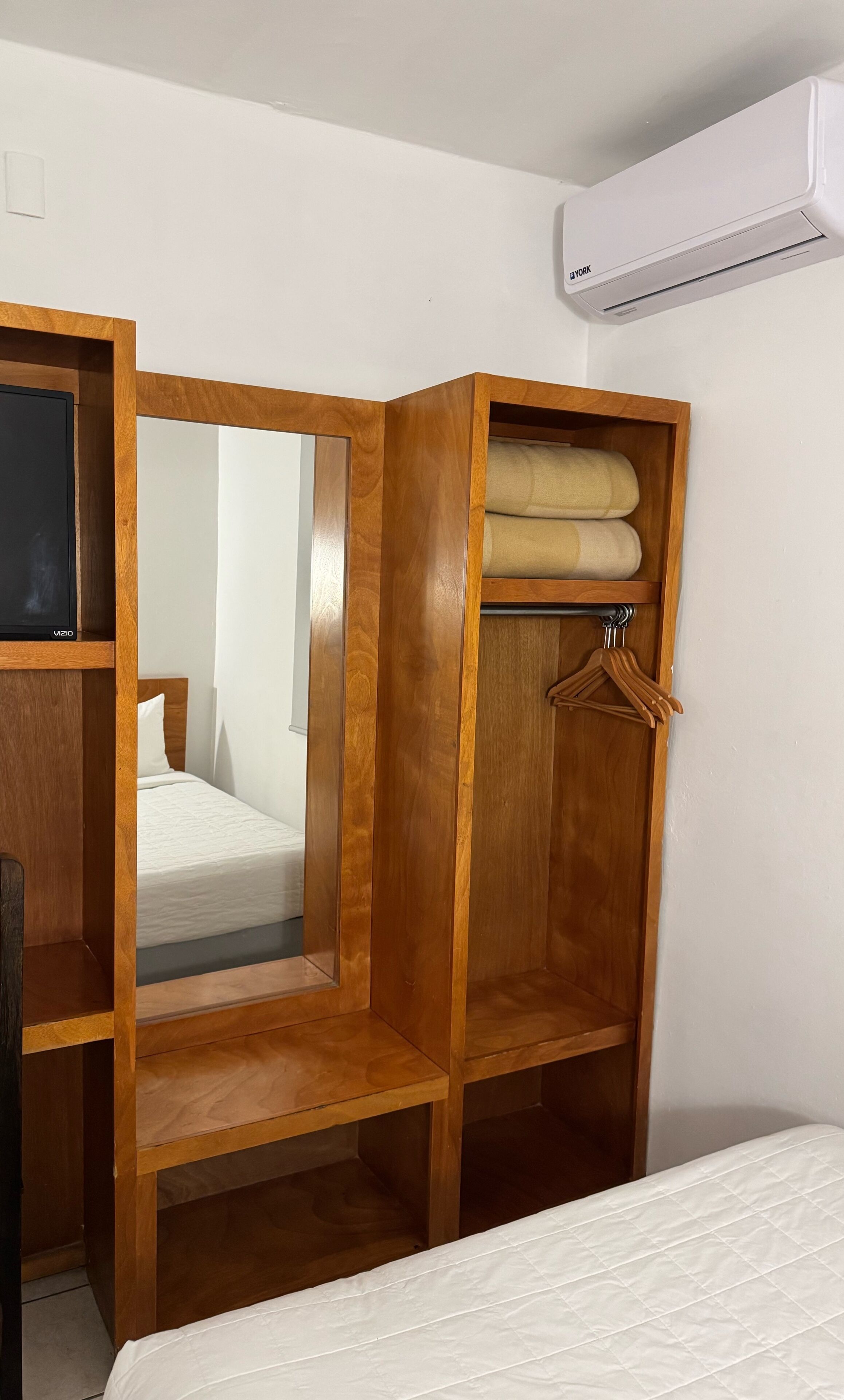 Un armadio in legno con specchio, un appendiabiti e un letto con copripiumino trapuntato bianco.