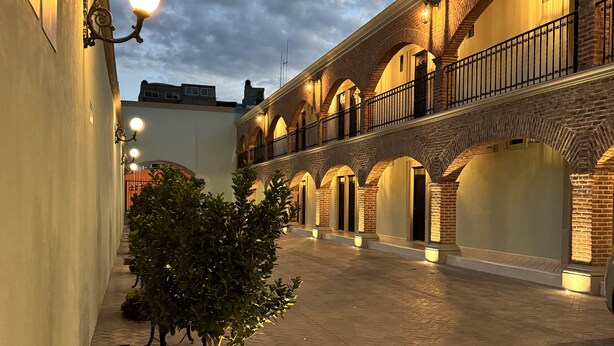 A courtyard with a brick building, arched walkways, and a tree. - Hotel Posada Real (Lagos de Moreno)