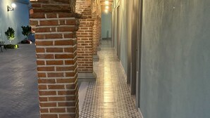 A corridor with patterned floor tiles, brick columns, and hanging lanterns. - Hotel Posada Real (Lagos de Moreno)