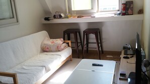 A small, cozy room with a white sofa, two wooden stools, a small table, and a TV. - OxbloodK (Gwangju)
