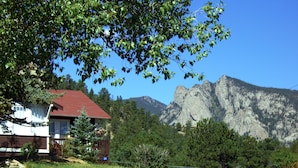 A house with a red roof, surrounded by a grassy area and a rocky outcrop. - River Rock Cottages (Estes Park)
