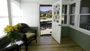 A room with a wicker chair, a vase with yellow flowers, and a view of a mountain through an open door. - River Rock Cottages (Estes Park)