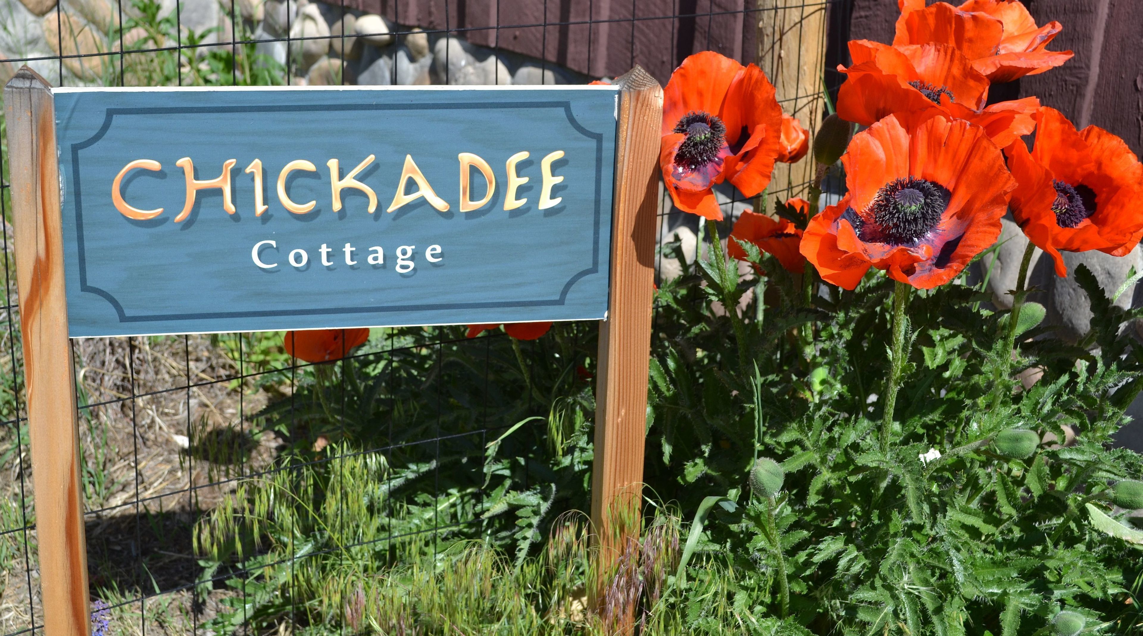 A sign for Chickadee Cottage with a wooden post and a blue background.