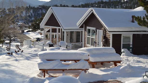 A cabin with a snow-covered deck and benches, surrounded by a snowy landscape and mountains. - River Rock Cottages (Estes Park)