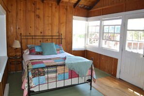 Ein Schlafzimmer mit Holzwänden, einem Bettgestell aus Metall, einer Steudecke und einem Fenster mit Blick auf ein Haus.