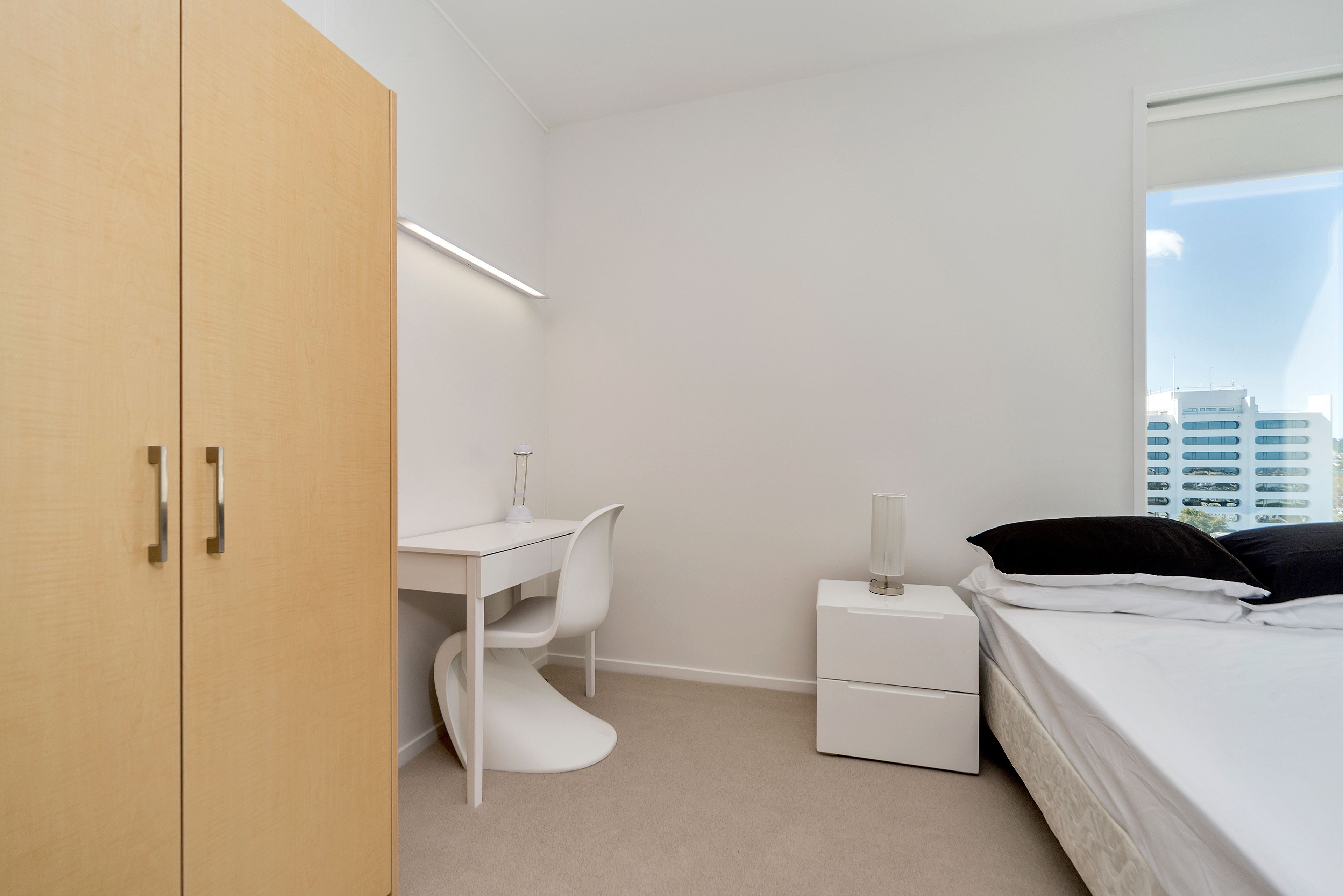 Un dormitorio con escritorio, silla, mesita de noche, lámpara y cama.