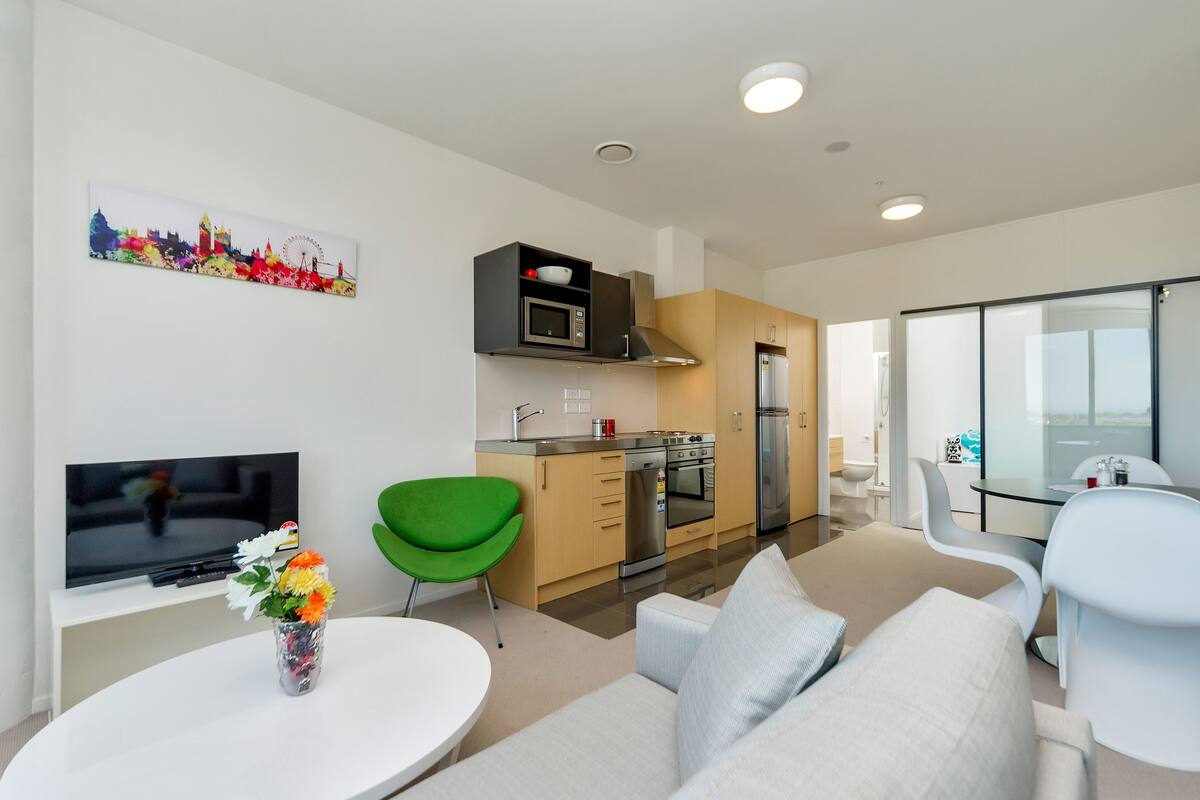 A modern living room with a flat-screen TV, a green chair, a sofa, and a dining table.