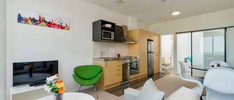 A modern living room with a flat-screen TV, a green chair, a sofa, and a dining table.